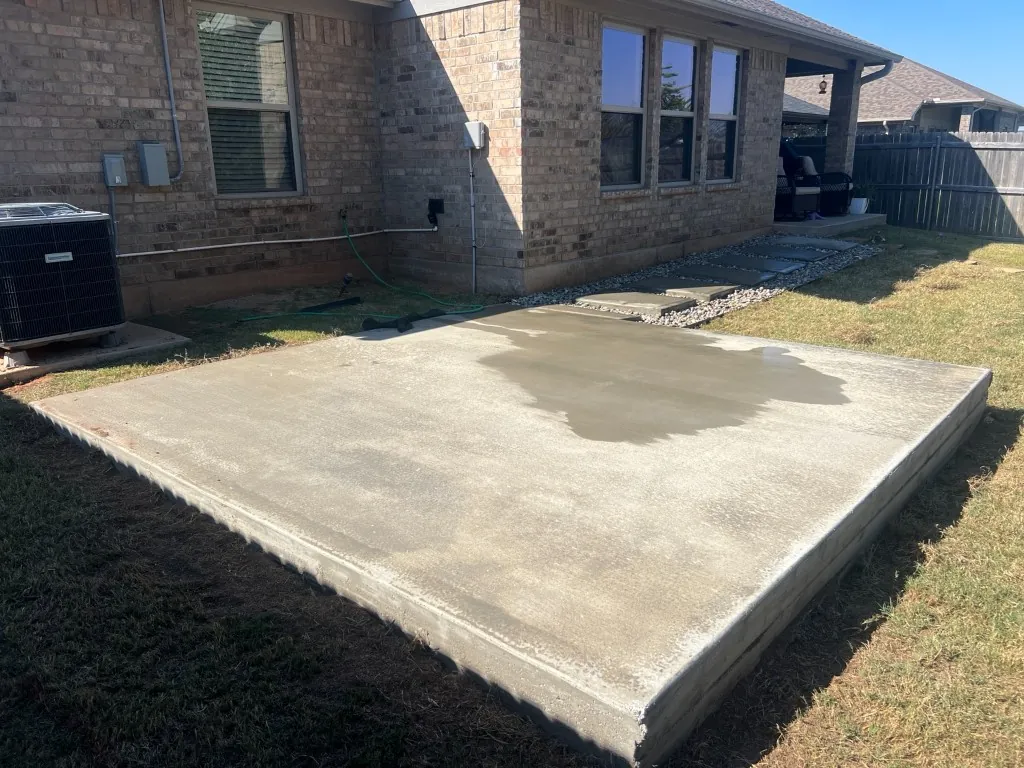 New 12 × 12 ft, 8-inch broom-finish concrete patio slab in a Norman, OK backyard