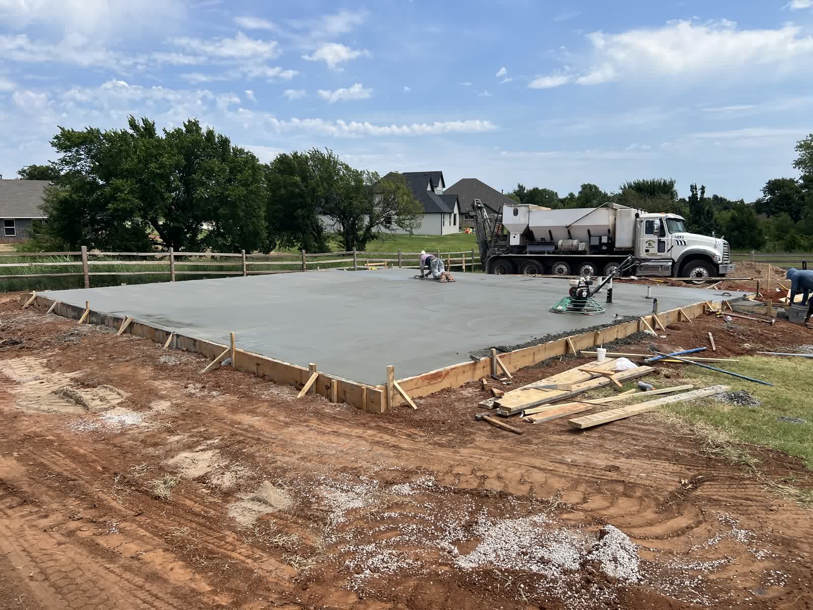 Concrete truck on site during pier foundation slab pour in Edmond, Oklahoma — crew finishing fresh slab